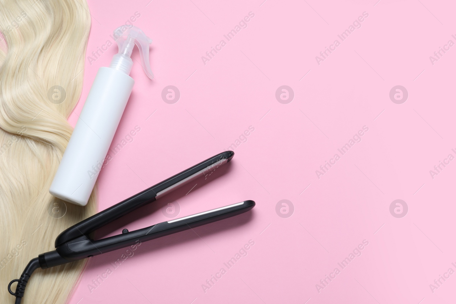 Photo of Spray bottle with thermal protection, iron and lock of blonde hair on pink background, flat lay. Space for text