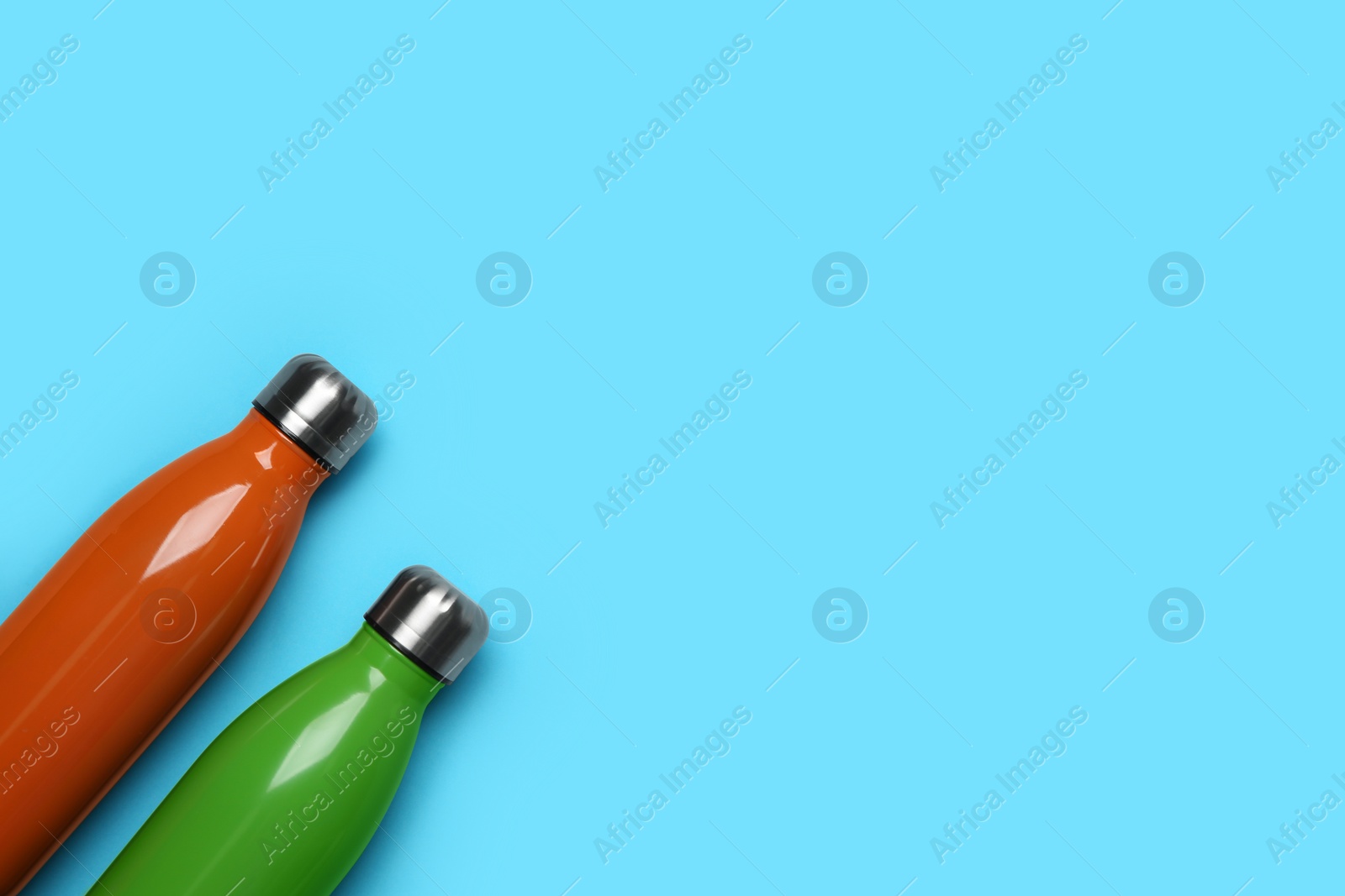 Photo of Modern thermo bottles on light blue background, flat lay. Space for text