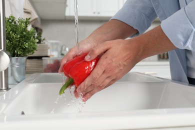 Man washing fresh bell pepper in kitchen, closeup