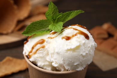 Photo of Scoops of tasty ice cream with caramel sauce and mint leaves on blurred background, closeup
