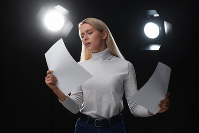 Casting call. Emotional woman with script performing on black background