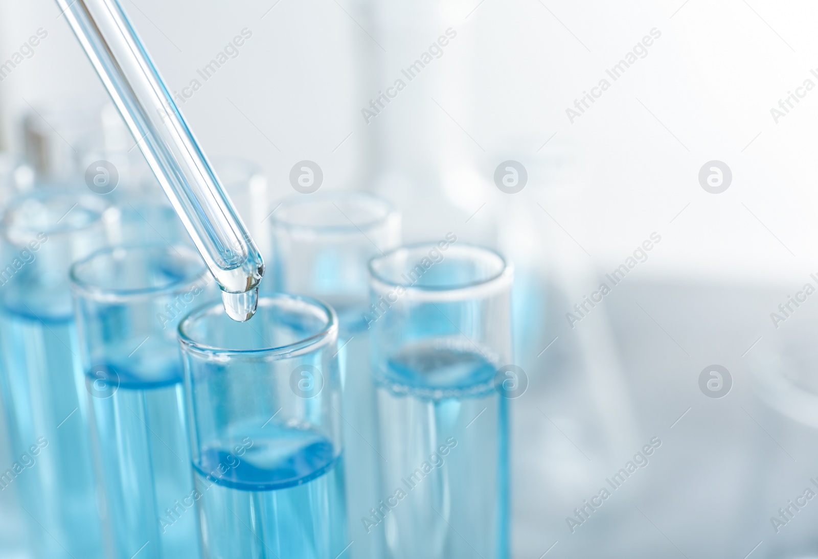 Photo of Dripping liquid from pipette into test tube on light background, closeup. Space for text