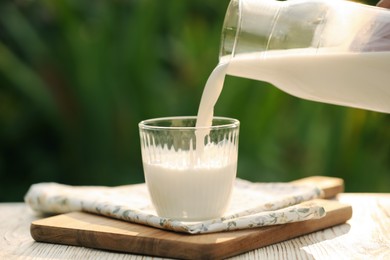 Photo of Pouring tasty fresh milk from bottle into glass on white wooden table, closeup