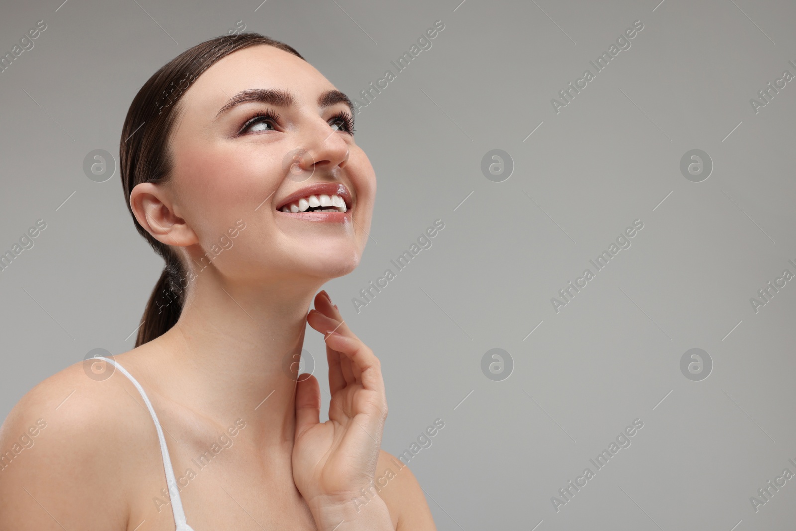 Photo of Smiling woman touching her neck on grey background. Space for text