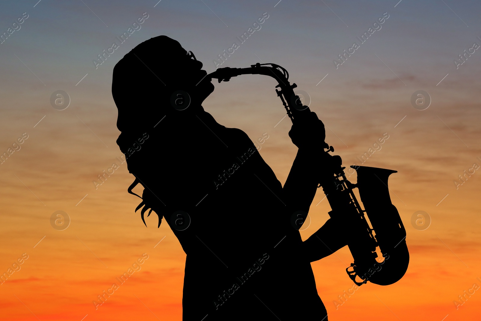 Image of Silhouette of woman playing saxophone against beautiful sky at sunset