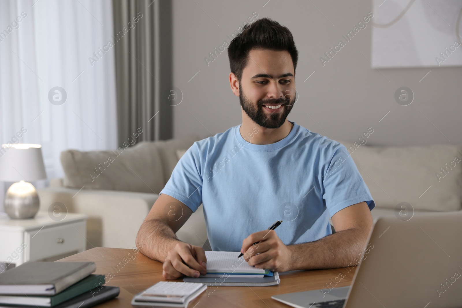 Photo of Young man watching webinar at table in room