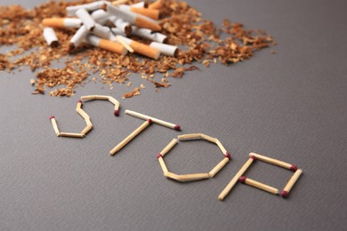 Photo of Word Stop made of matches, broken cigarettes and dry tobacco on dark grey background. Quitting smoking concept