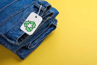 Photo of Jeans with recycling label on yellow background. Space for text