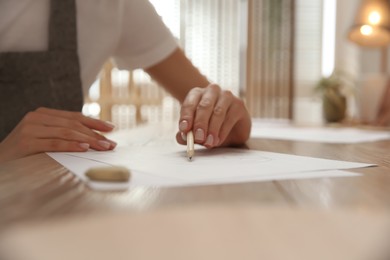 Photo of Young woman drawing with pencil at table indoors, closeup