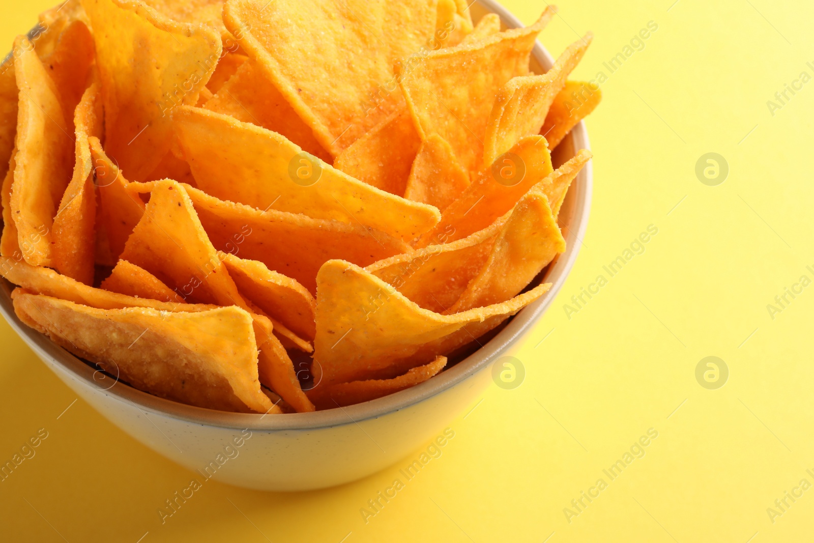 Photo of Tortilla chips (nachos) in bowl on yellow background, closeup