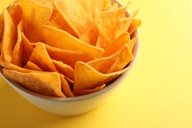 Photo of Tortilla chips (nachos) in bowl on yellow background, closeup