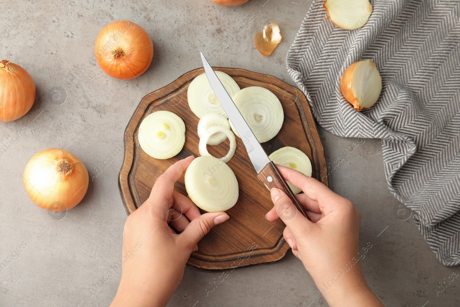 Photo of Young woman cutting ripe onion on wooden board at grey table, top view