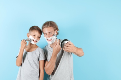 Photo of Father and son shaving together on color background, space for text