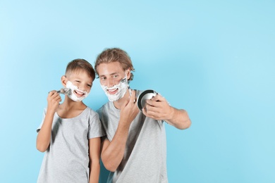 Father and son shaving together on color background, space for text