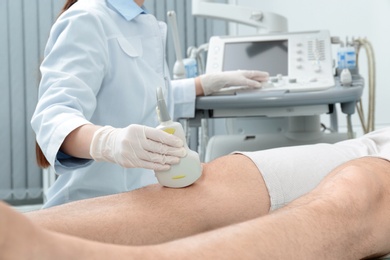 Doctor conducting ultrasound examination of patient's knee in clinic