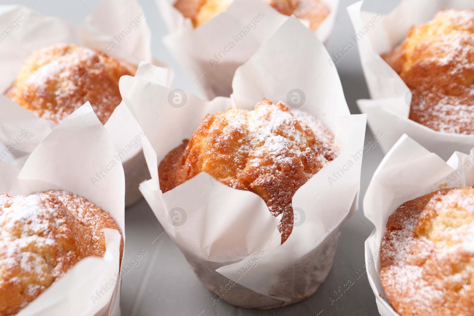 Photo of Delicious muffins with powdered sugar on grey table, closeup