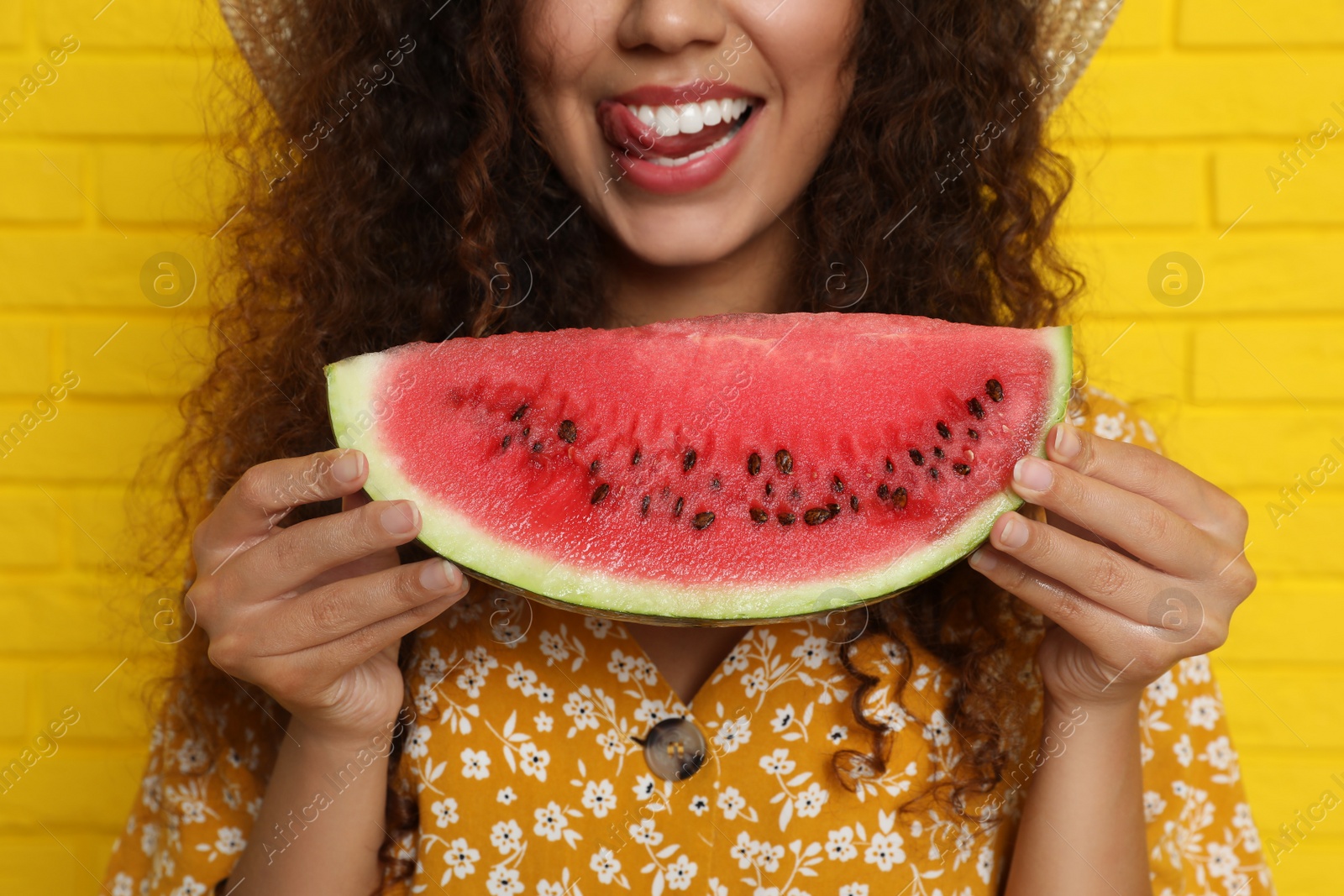 Photo of Beautiful young African American woman with watermelon near yellow brick wall, closeup