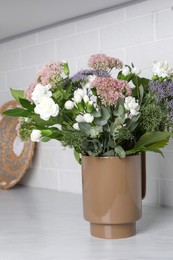 Photo of Ceramic vase with beautiful bouquet on light table near white brick wall