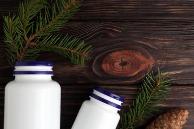 Photo of White medical bottles, spruce twigs and cone on wooden table, flat lay