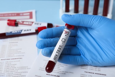 Scientist holding tube with blood sample and label HIV Test near laboratory form, closeup