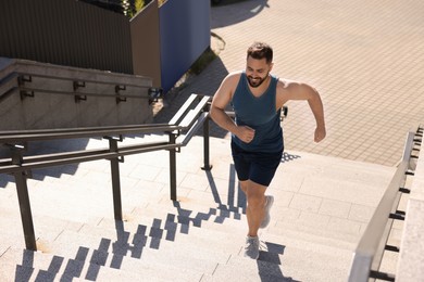 Smiling man running up stairs outdoors on sunny day, above view. Space for text