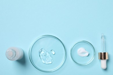 Photo of Petri dishes with samples of cosmetic serums, bottle and pipette on light blue background, flat lay. Space for text