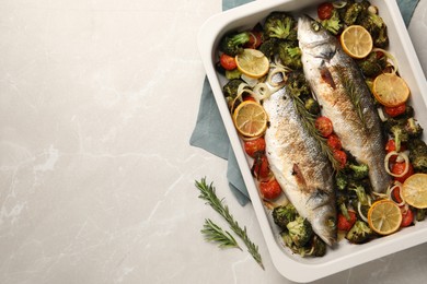 Delicious fish with vegetables and lemon in baking dish on light marble table, top view. Space for text