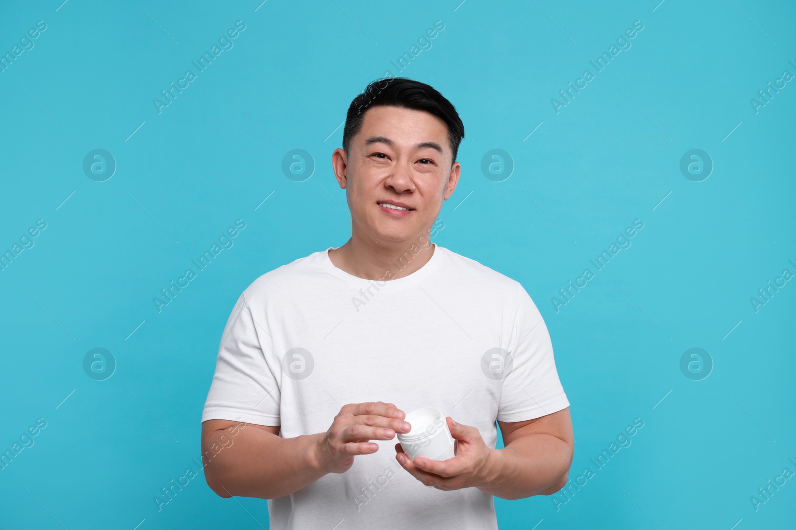 Photo of Handsome man with jar of body cream on light blue background