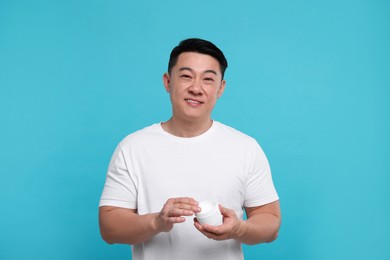 Photo of Handsome man with jar of body cream on light blue background