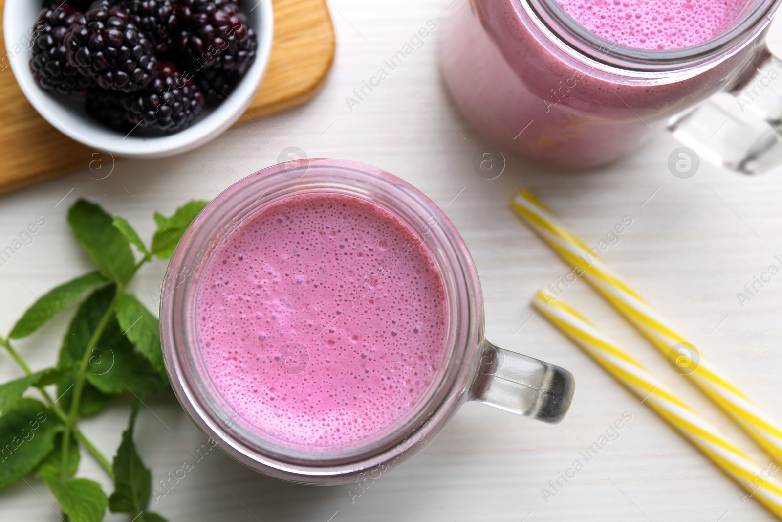 Photo of Mason jar of blackberry smoothie, mint and berries on white wooden table, flat lay