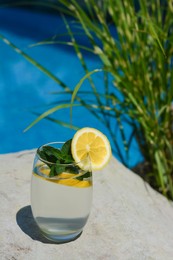 Photo of Refreshing water with lemon and mint on rock outdoors