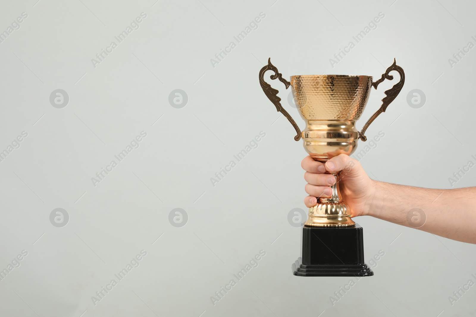 Photo of Man holding gold trophy cup on light grey background, closeup. Space for text