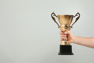 Photo of Man holding gold trophy cup on light grey background, closeup. Space for text