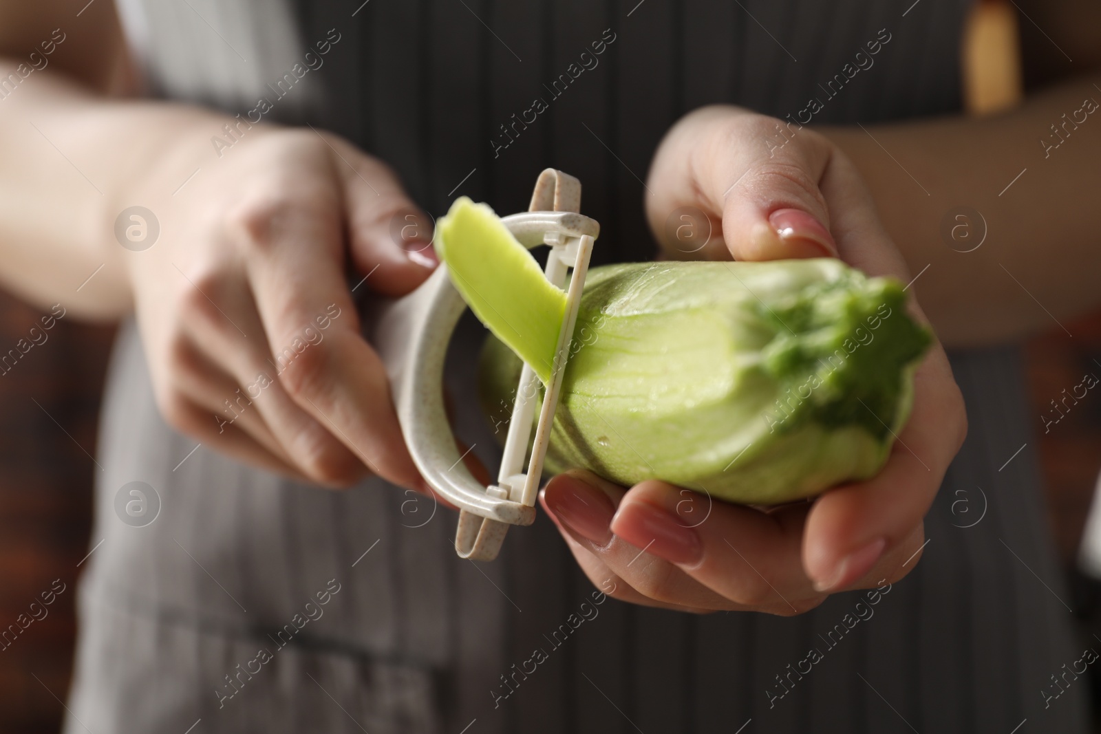 Photo of Woman peeling fresh zucchini indoors, closeup view