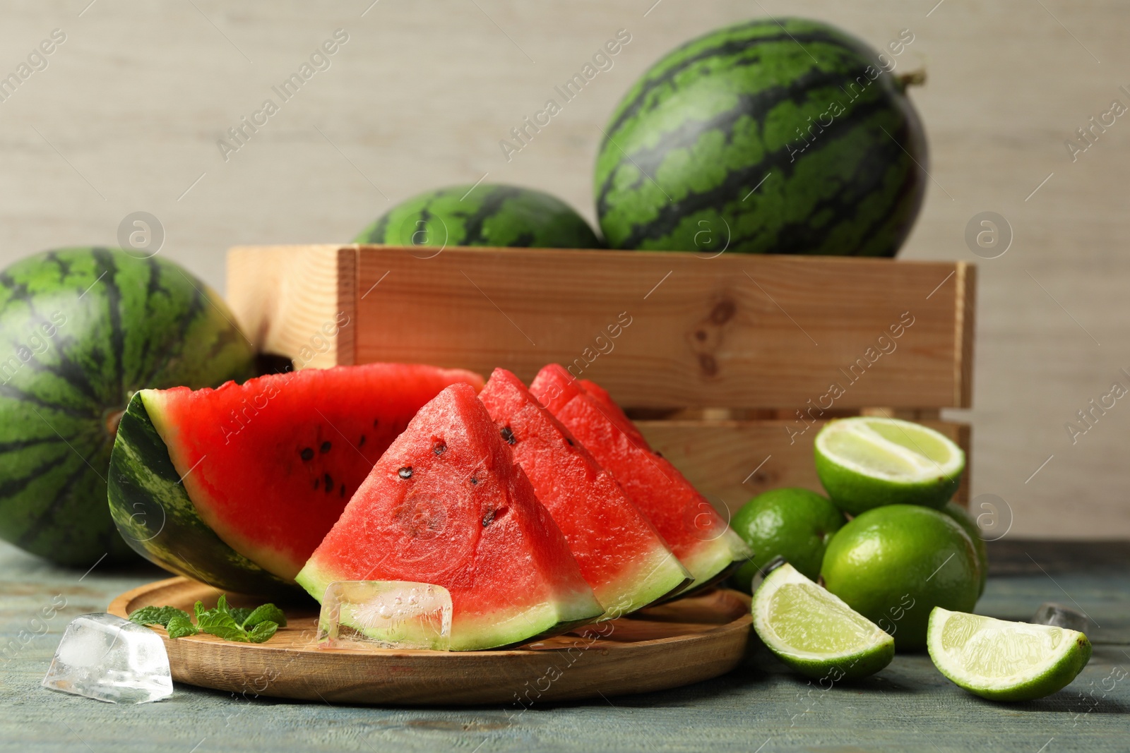 Photo of Slices of delicious watermelon, limes, ice and mint on light blue wooden table