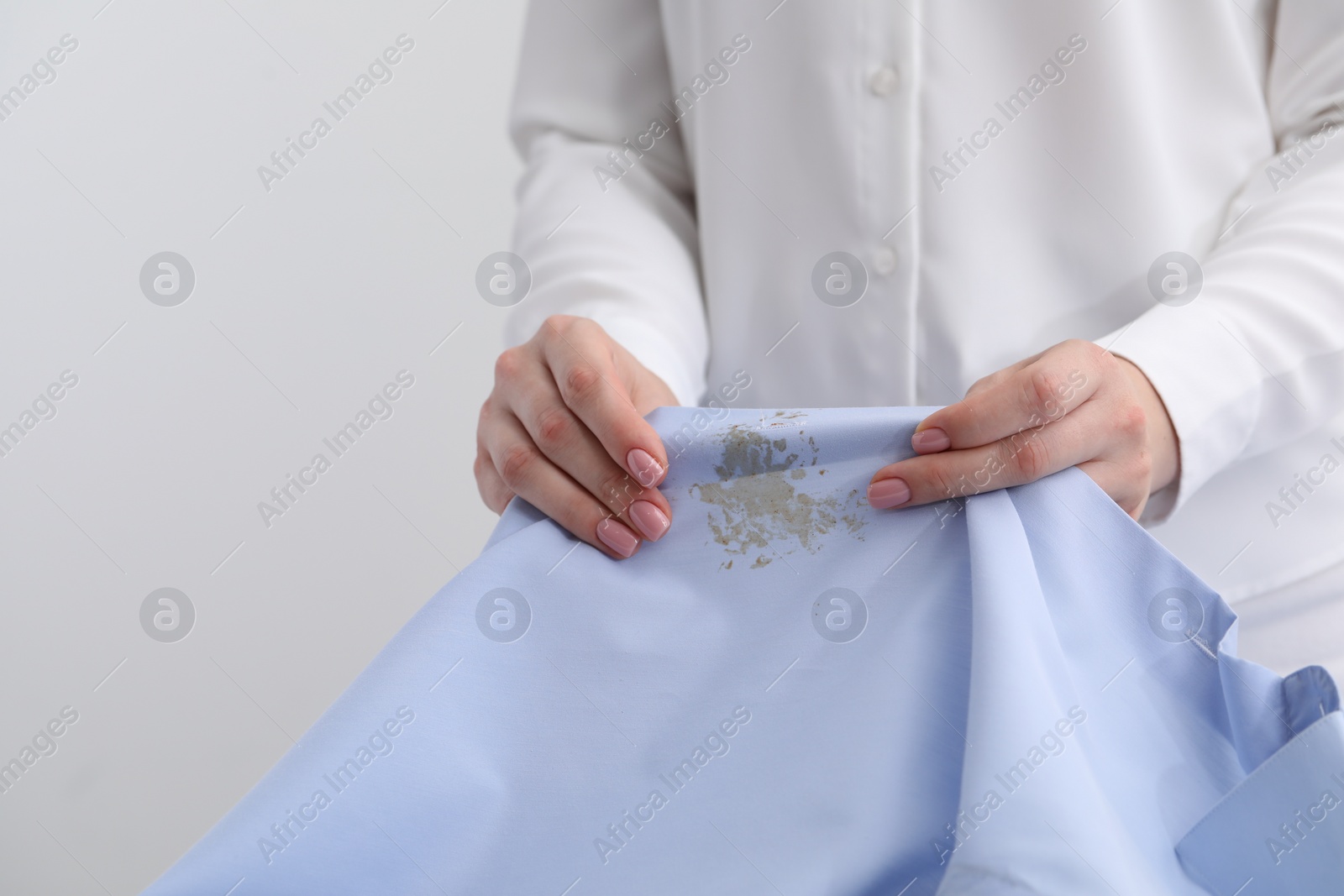 Photo of Woman holding shirt with stain against light background, closeup