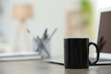 Photo of Black ceramic mug and laptop on wooden table indoors