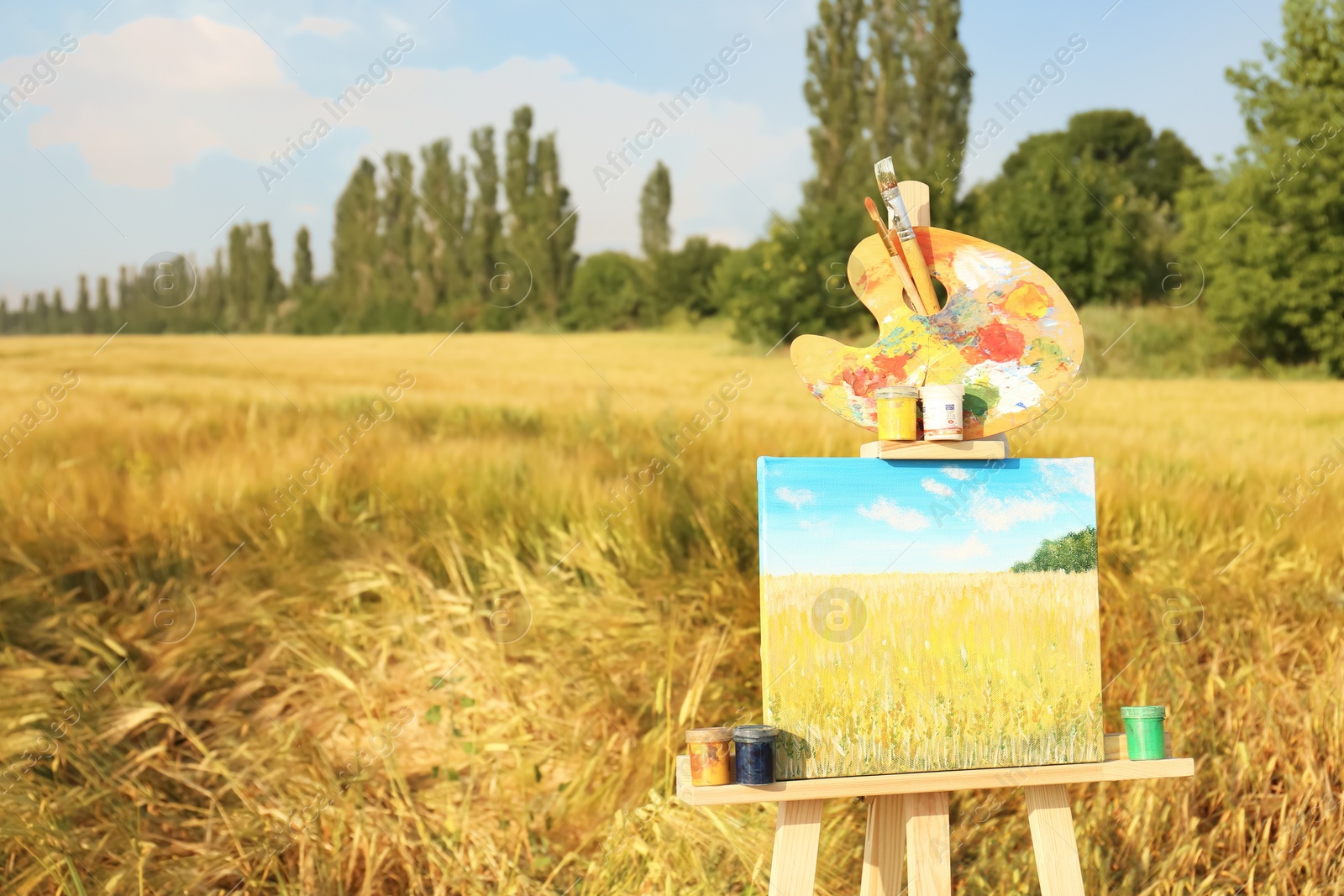 Photo of Wooden easel with beautiful picture and painting equipment in field. Space for text