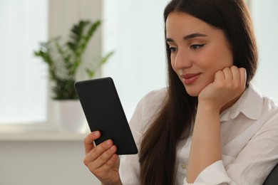 Photo of Young woman using e-book reader at home