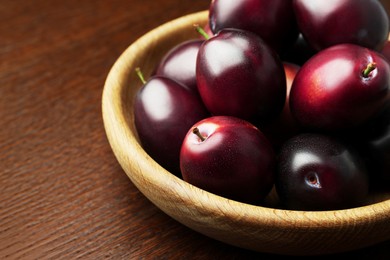 Bowl with tasty ripe plums on wooden table, closeup