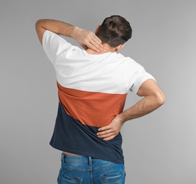 Photo of Young man suffering from back pain on grey background