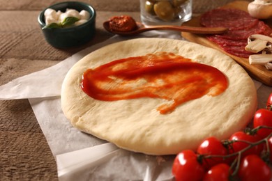 Photo of Pizza dough with tomato sauce and products on wooden table, closeup