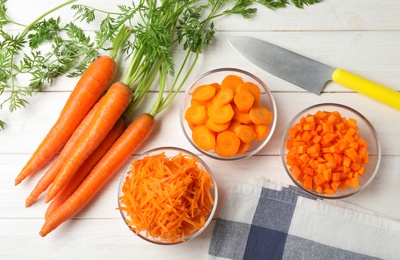 Photo of Bowls of differently cut carrots on white background, flat lay