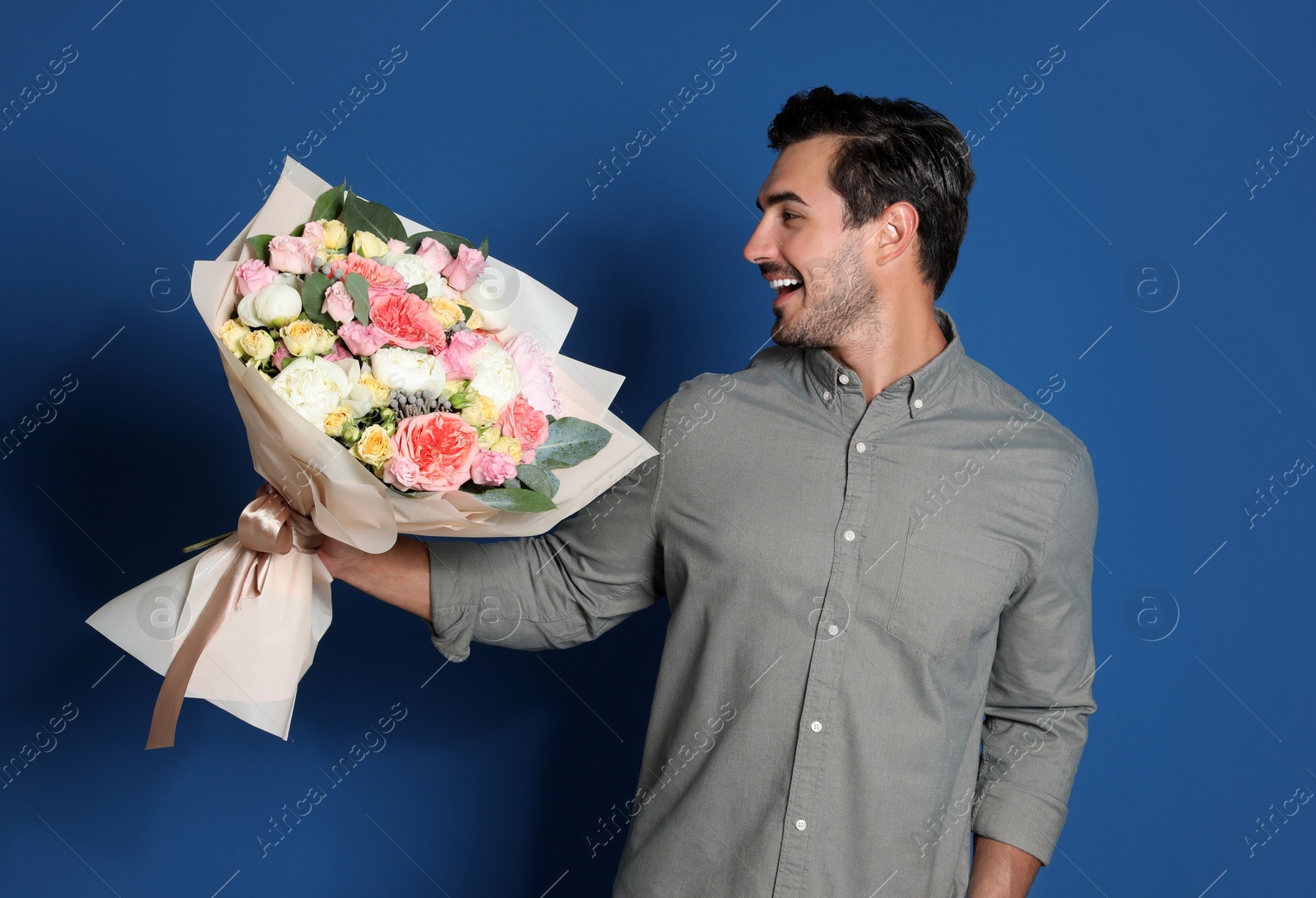 Photo of Young handsome man with beautiful flower bouquet on blue background