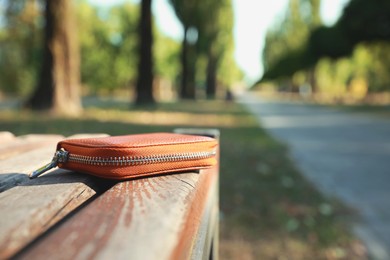 Brown leather purse on wooden bench outdoors, space for text. Lost and found