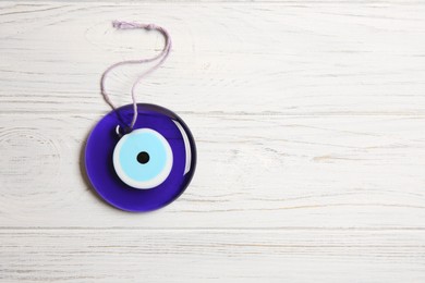 Photo of Evil eye amulet on white wooden table, top view. Space for text