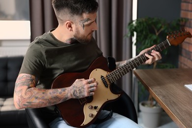 Photo of Handsome hipster man playing guitar in stylish room