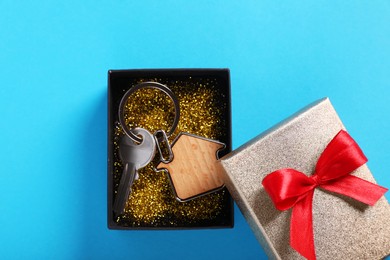 Photo of Key with trinket in shape of house and gift box on light blue background, flat lay. Housewarming party
