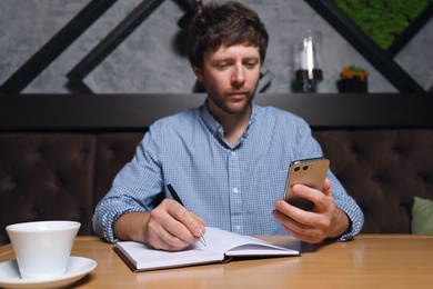 Photo of Handsome man using smartphone at table in cafe