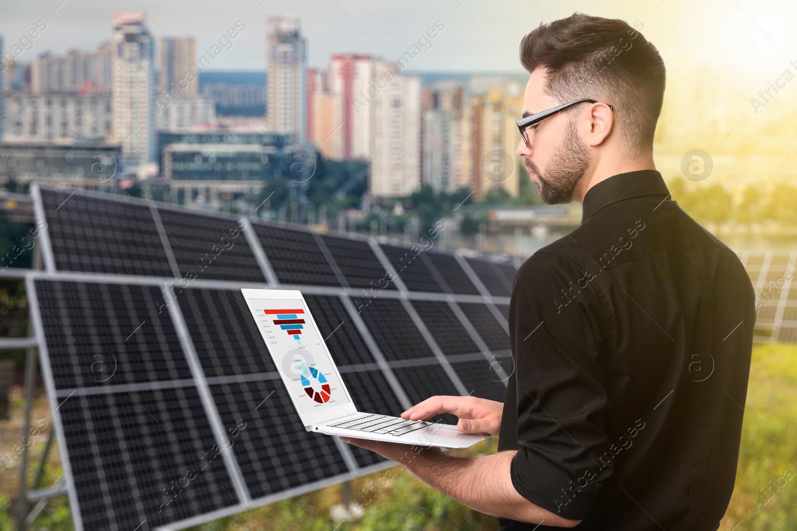 Image of Young businessman with laptop near solar panels and beautiful view of cityscape. Alternative energy source